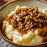 Ground beef and gravy served over fluffy mashed potatoes in a bowl.